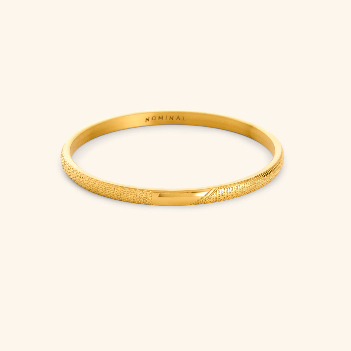 Gold keffiyeh pattern engraved bangle with 'NOMINAL' branding on a light background.