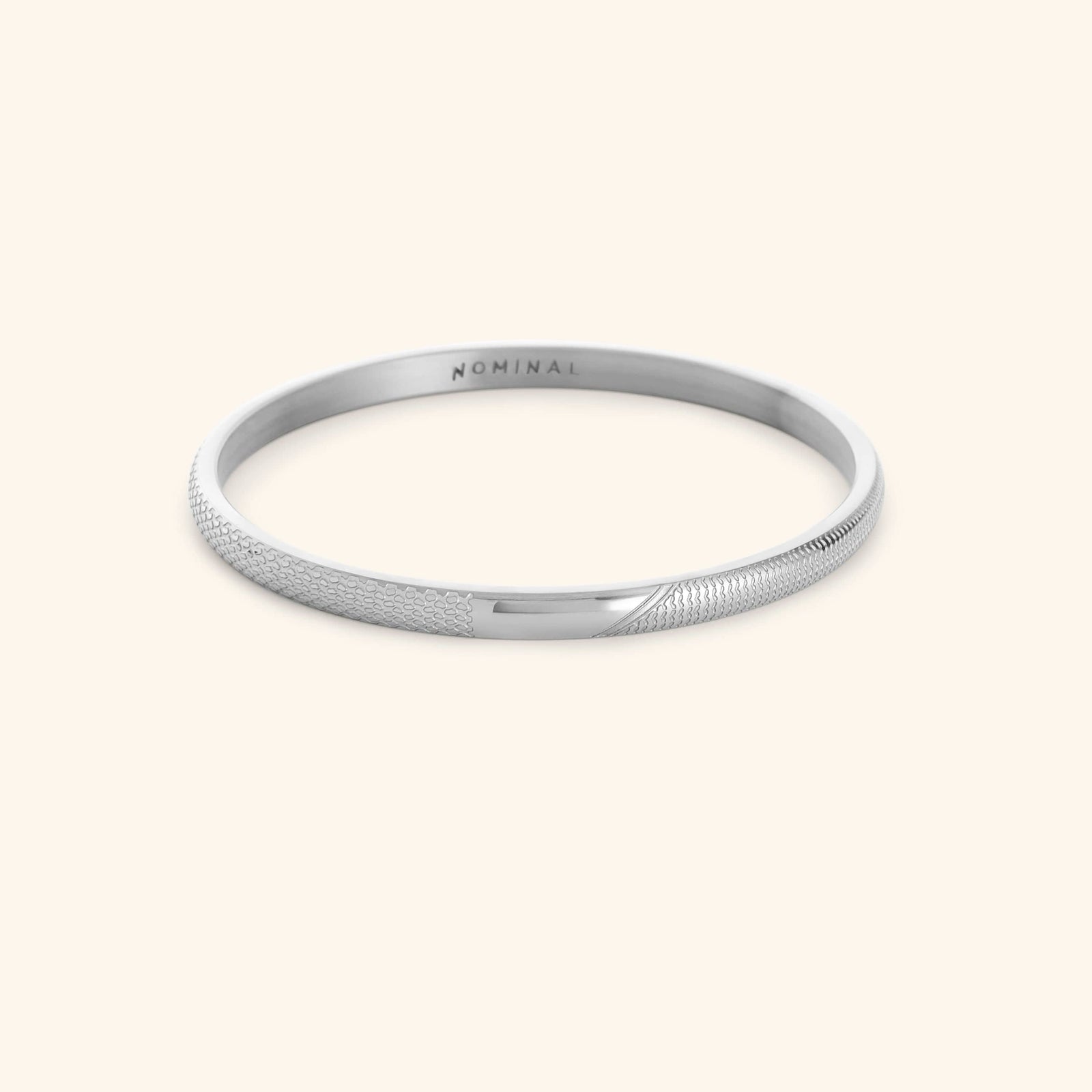 Silver keffiyeh pattern engraved bangle with NOMINAL branding on a light background.