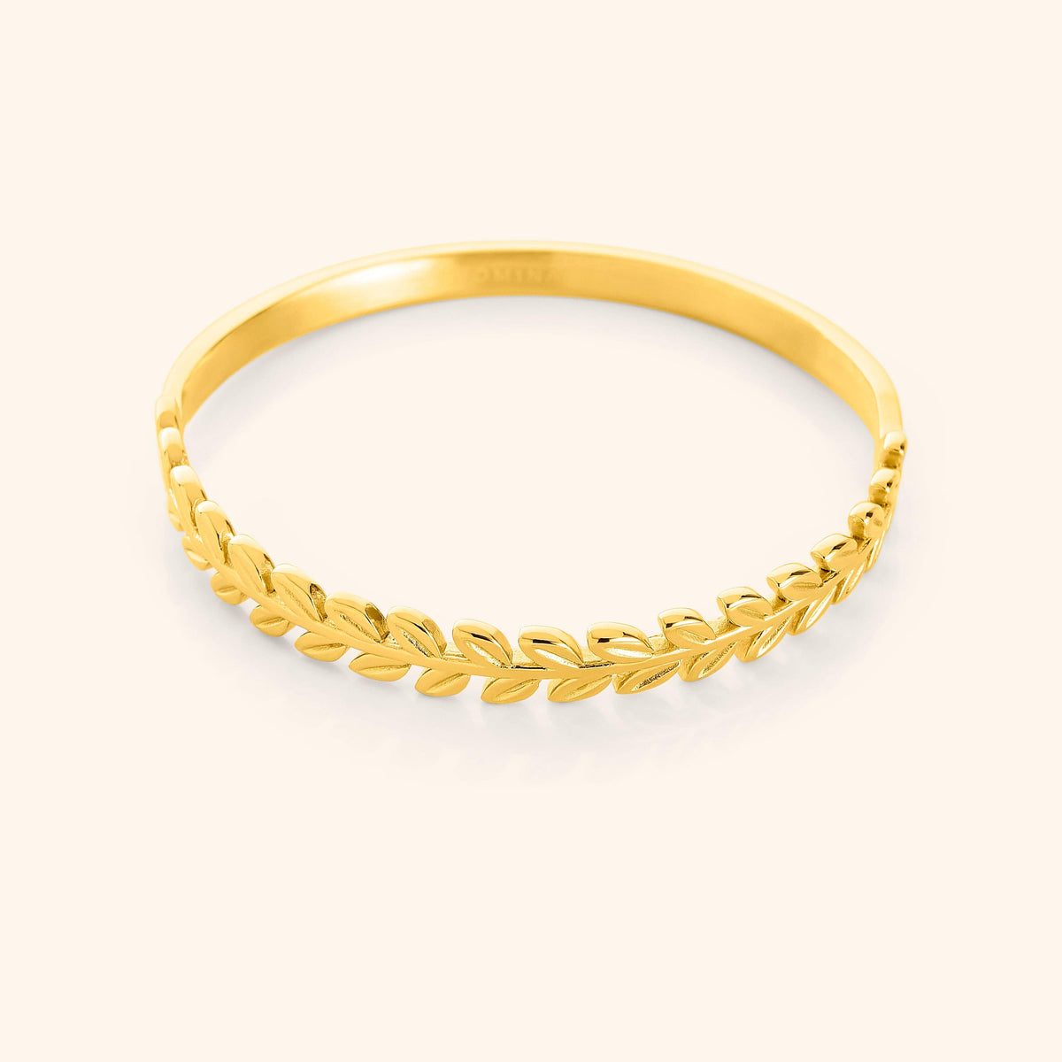 A close-up of the Palestine Olive Layering Bangle in 18K gold plating. The bangle features a delicately twisted olive branch design along one half, symbolizing peace and strength, while the other half remains sleek and unadorned for a modern balance.