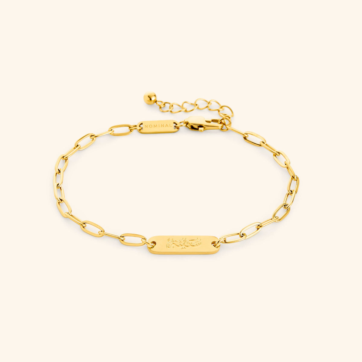 Gold Sakinah Serenity link bracelet showing the Arabic engraving on center tag, photographed against a light background.