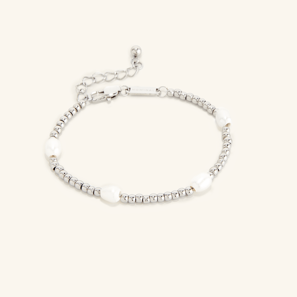 Gold bracelet with small round beads and five evenly spaced white pearls, shown on a cream background with an adjustable clasp and extender chain engraved with 'NOMINAL'.
