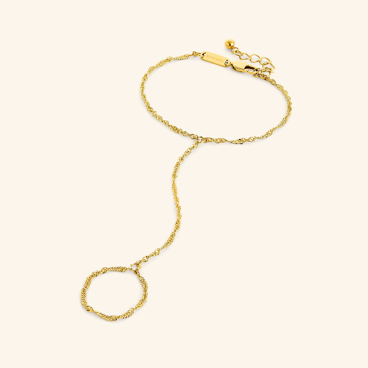 Flat lay of a gold twisted hand chain, extending from bracelet to ring loop, and clasp engraved with “NOMINAL.”