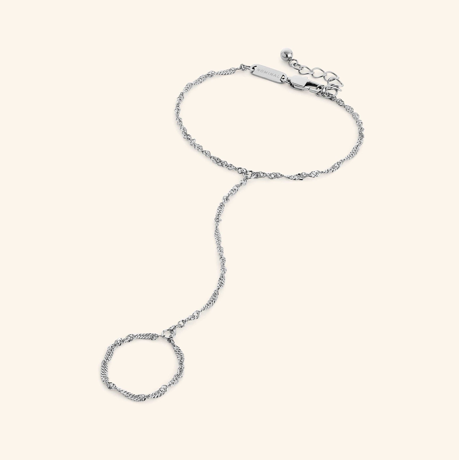 Flat lay of a silver twisted hand chain, extending from bracelet to ring loop, and clasp engraved with “NOMINAL.”