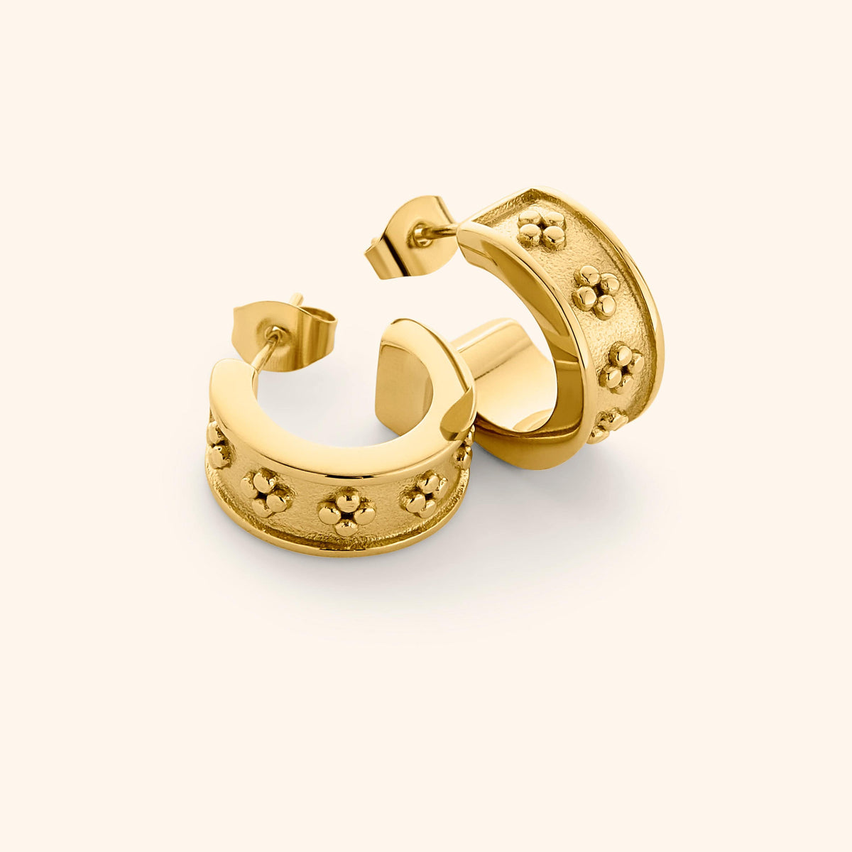 Flat lay of gold Henna Hoops, featuring wide curved band with raised dotted floral motifs on a textured surface.