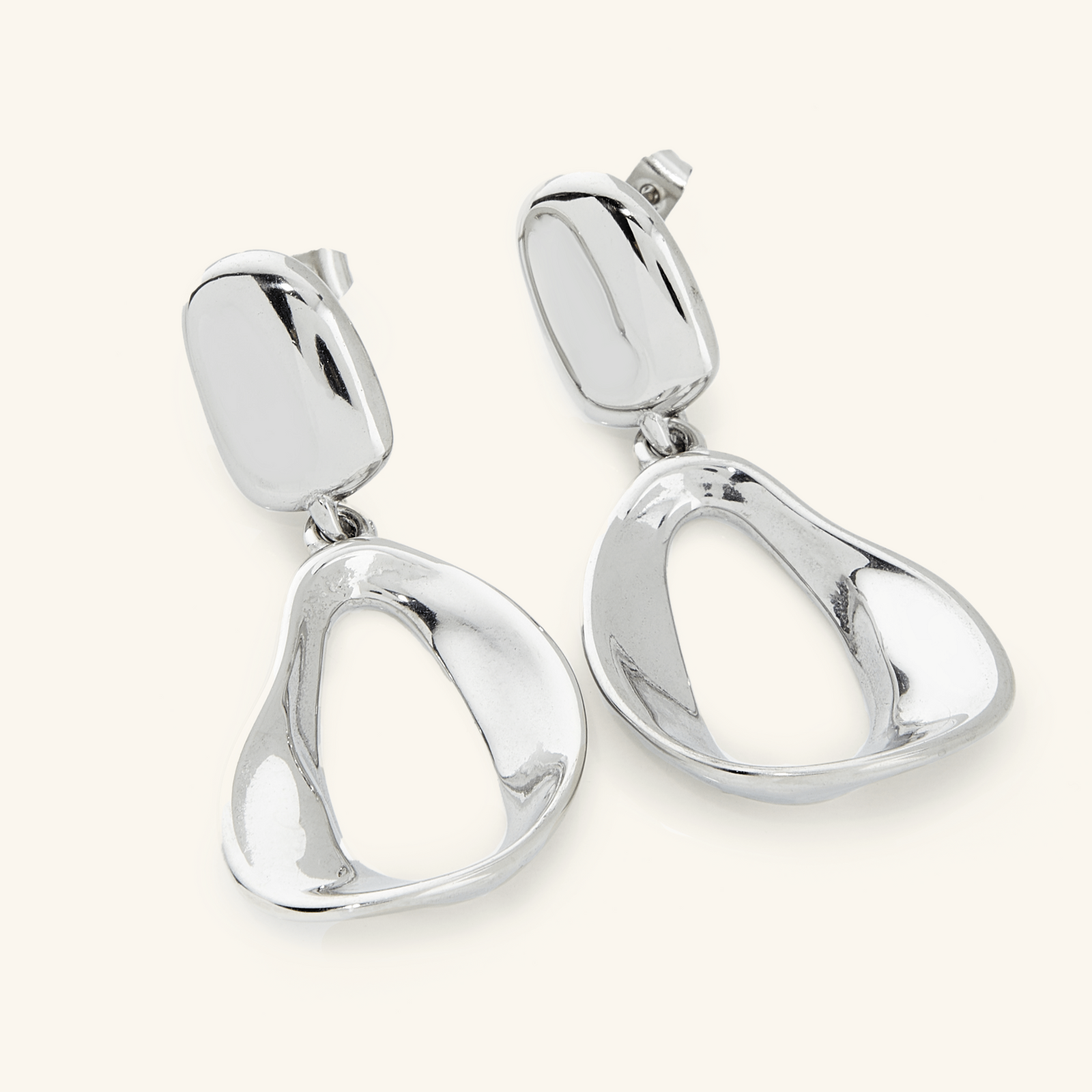 A pair of silver earrings. The Droop Earrings features a design that is held by a melted stud and then dropping into statement-like melting oval hoops 