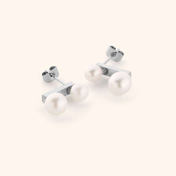 Silver stud earrings with two different sized pearls, shot on a light background