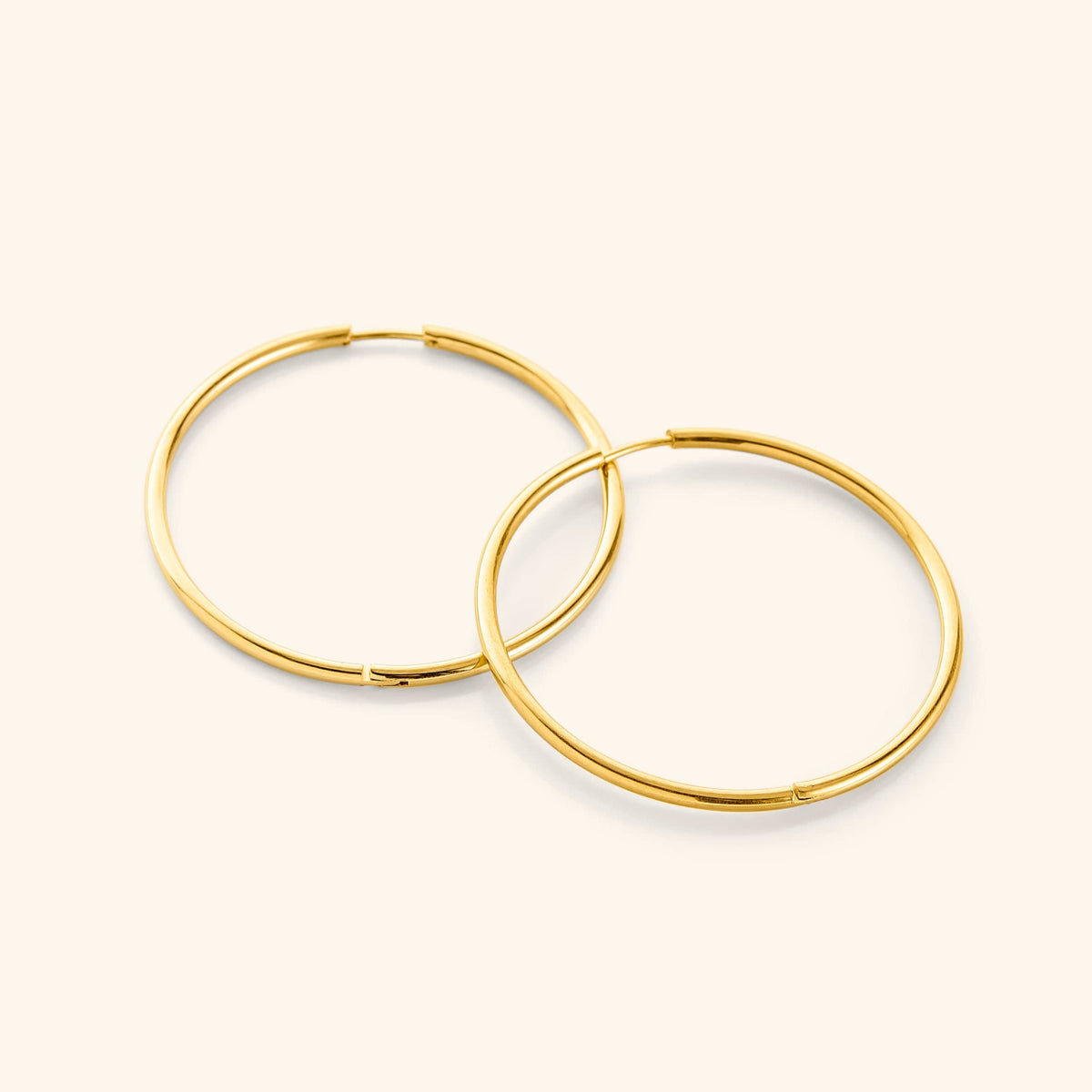 Flat lay of a pair of 18k gold plated Oversized Essential Hoops | 40mm against a light background.