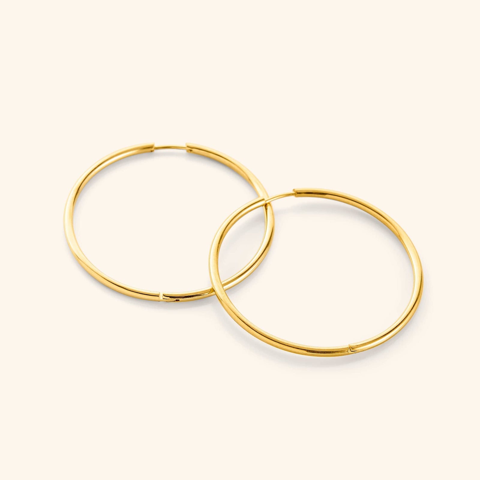 Flat lay of a pair of 18k gold plated Oversized Essential Hoops | 40mm against a light background.