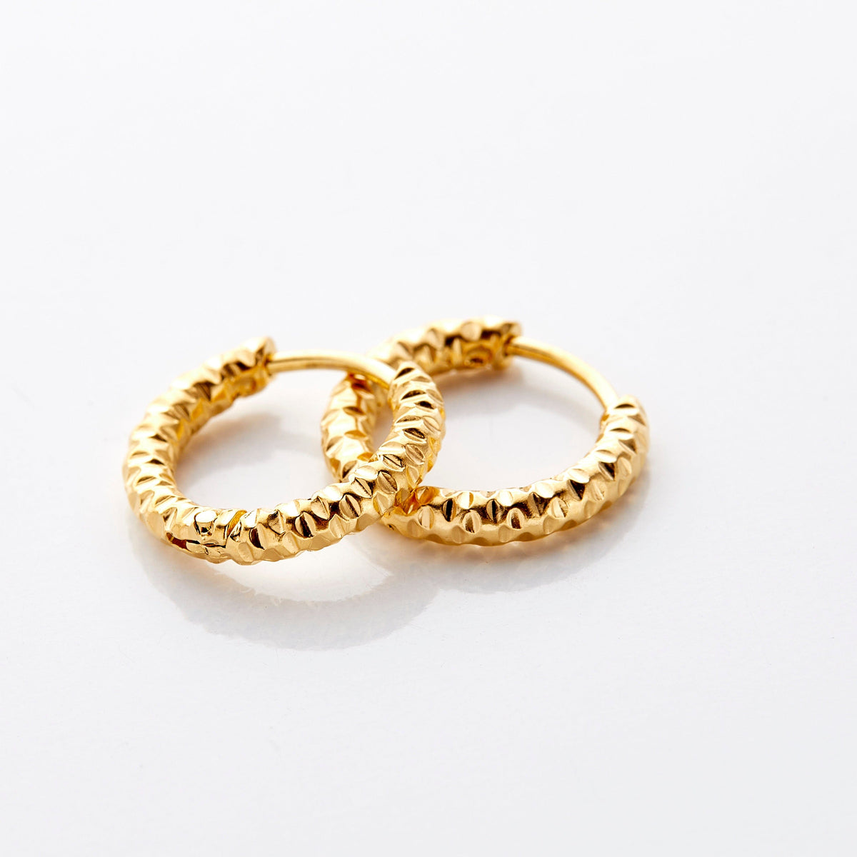 Photo of a pair of 18k gold plated hoop earrings. The Flake Hoops have the silhouette of classic hoops, with an added flair in its imperfect edges that give it a glowing vintage.