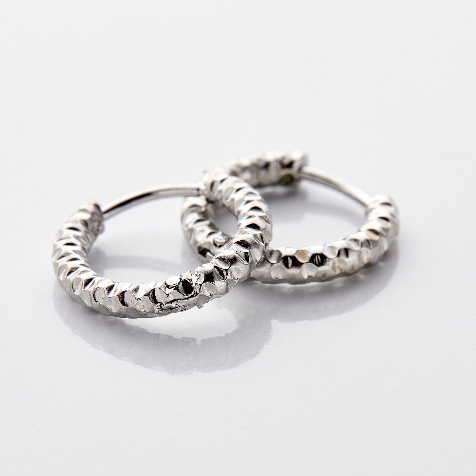 Photo of a pair of silver hoop earrings. The Flake Hoops have the silhouette of classic hoops, with an added flair in its imperfect edges that give it a glowing vintage.