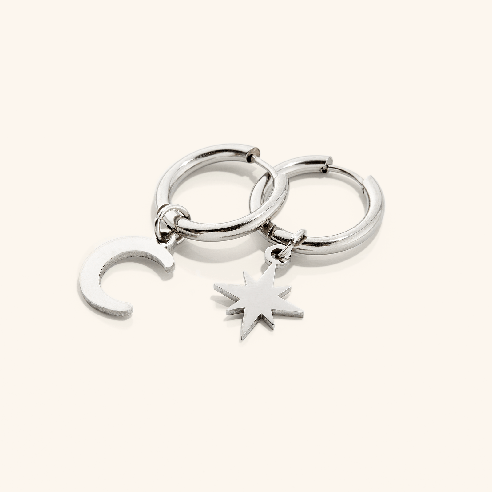 A pair of silver hoop earring, one piece features a star charm and the other, a crescent moon charm.