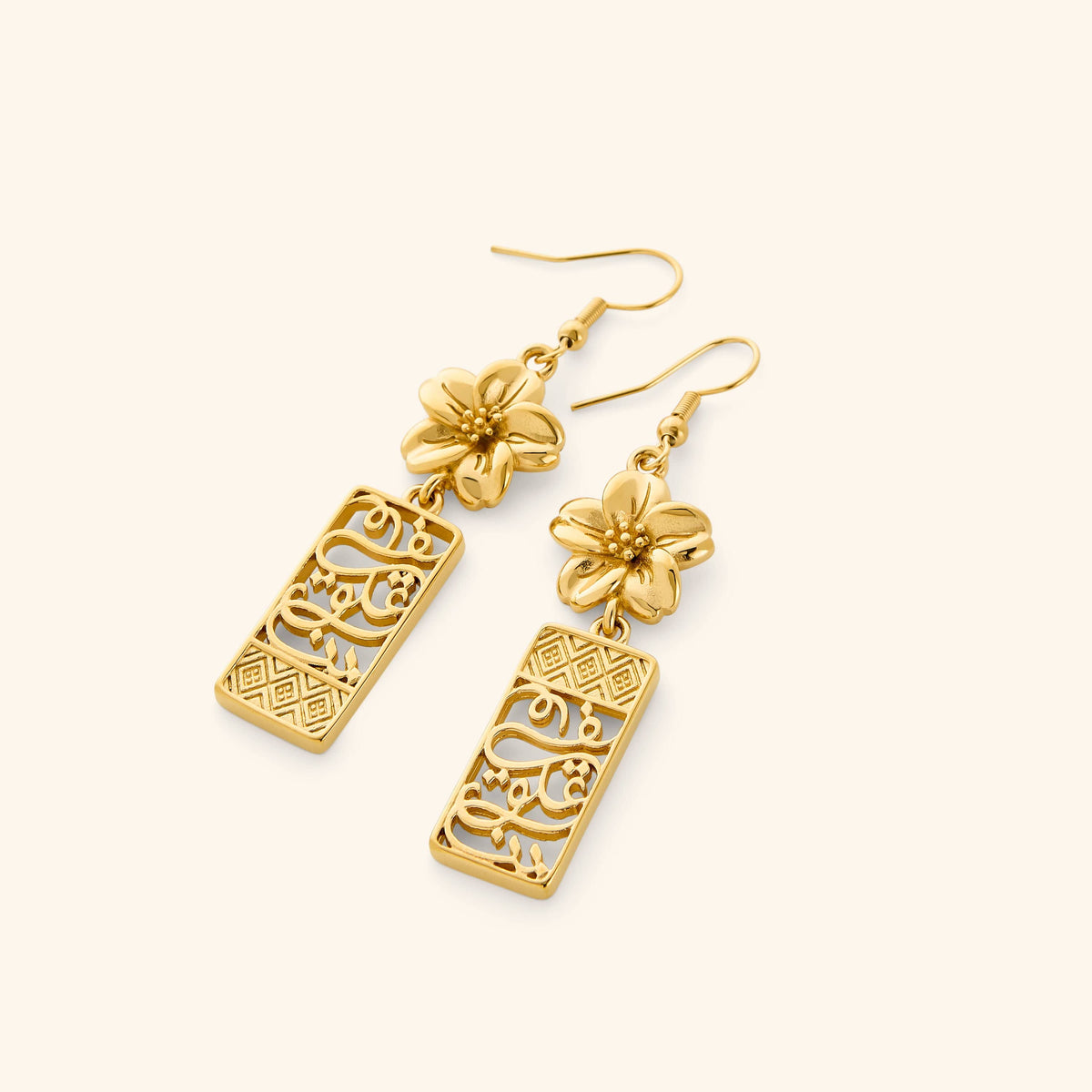 A pair of gold dangling earrings featuring patterns found in the Damascus masjids and courtyards and Arabic calligraphy "in our hearts" design finished with blooming petals of a Jasmine at the top.
