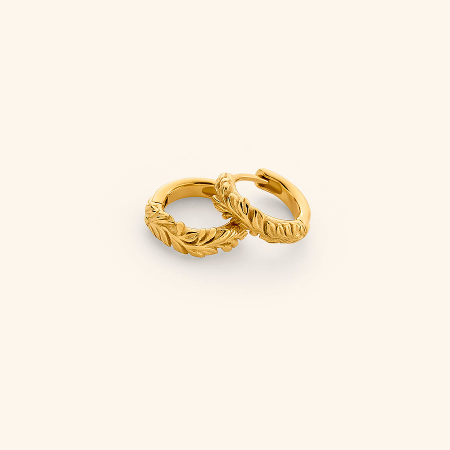 The Palestinian Olive Huggie Hoops by Nominal, featuring intricate embossed olive branch leaf detailing on 18k gold-plated hoop earrings, displayed on an off-white background.