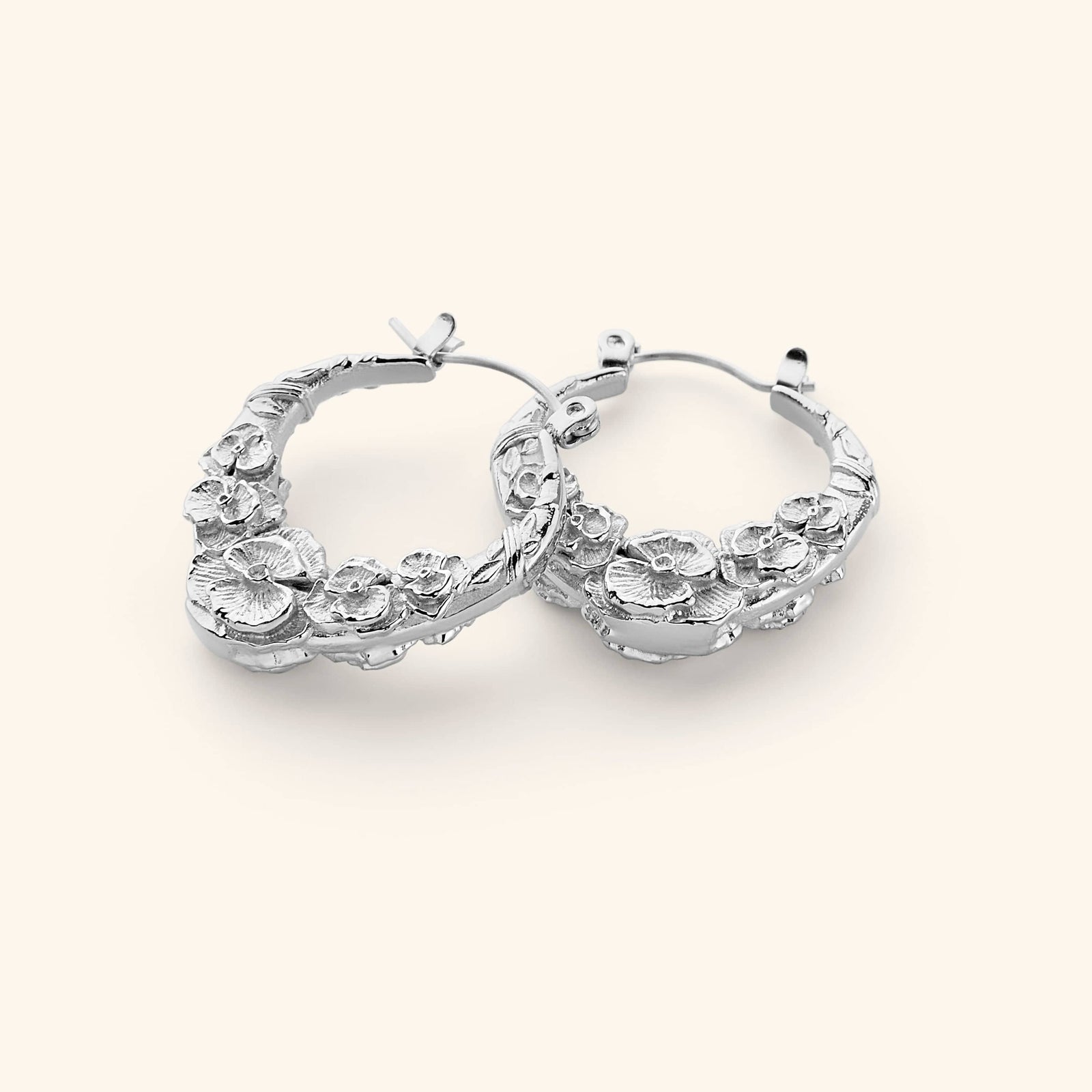 A pair of silver hoop earrings that feature sculpted poppy flower design.