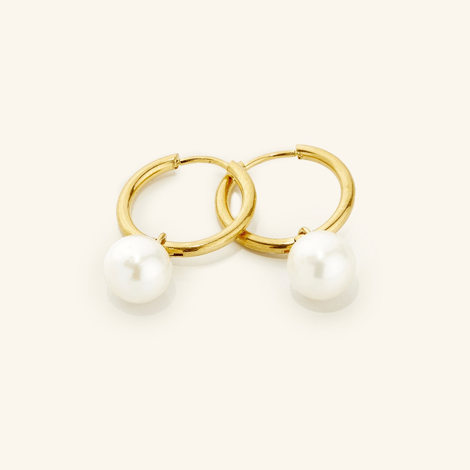 a pair of 18k gold plated earrings laid flat against a light background. The Pearl Hoops are made with real freshwater pearls hanging from minimal hoops