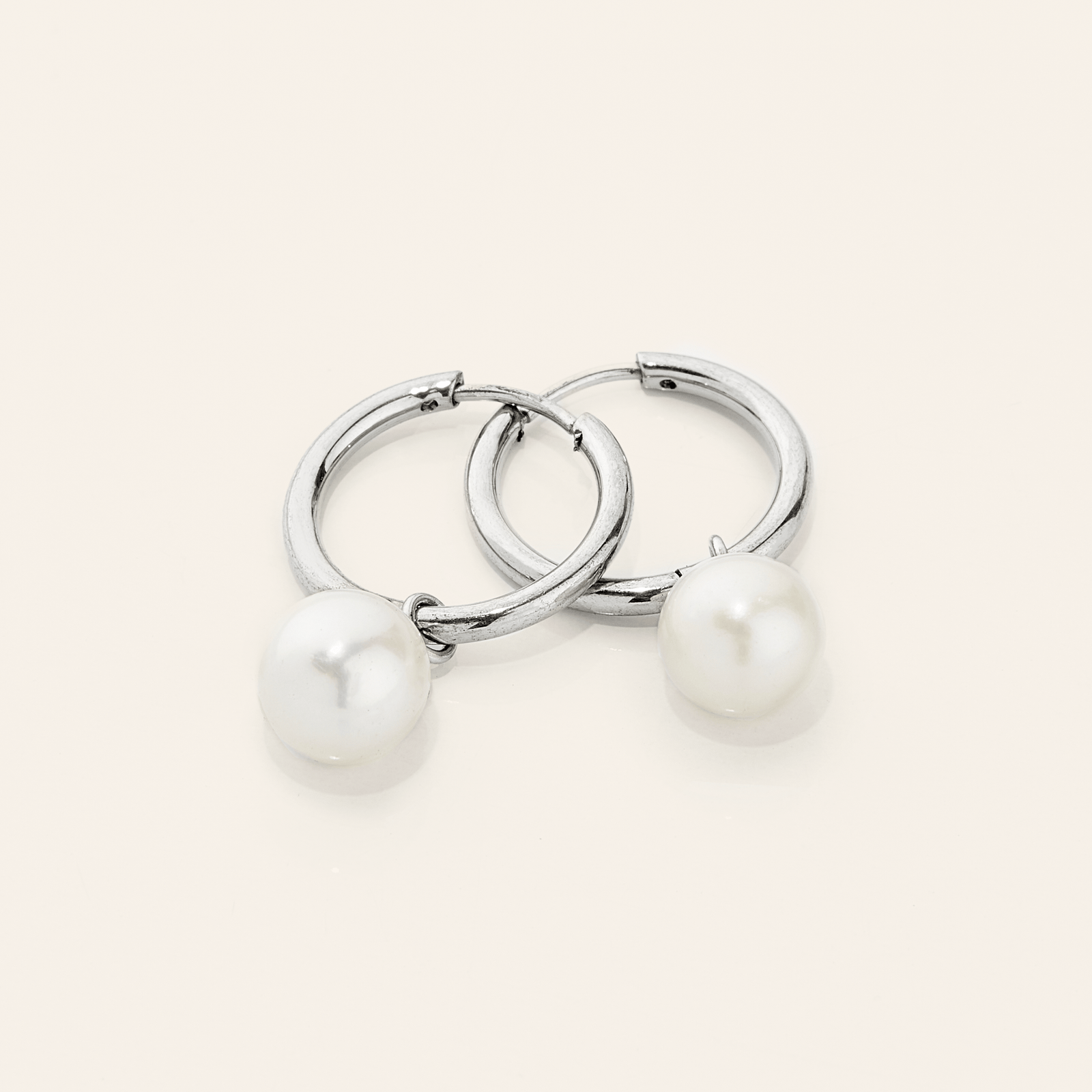 a pair of silver earrings laid flat against a light background. The Pearl Hoops are made with real freshwater pearls hanging from minimal hoops