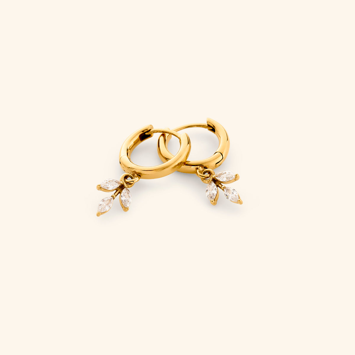 The Pavé Olive Branch Huggies by Nominal, featuring smooth 18k gold-plated hoop earrings with dangling marquise crystal olive leaf charms, displayed on an off-white background.
