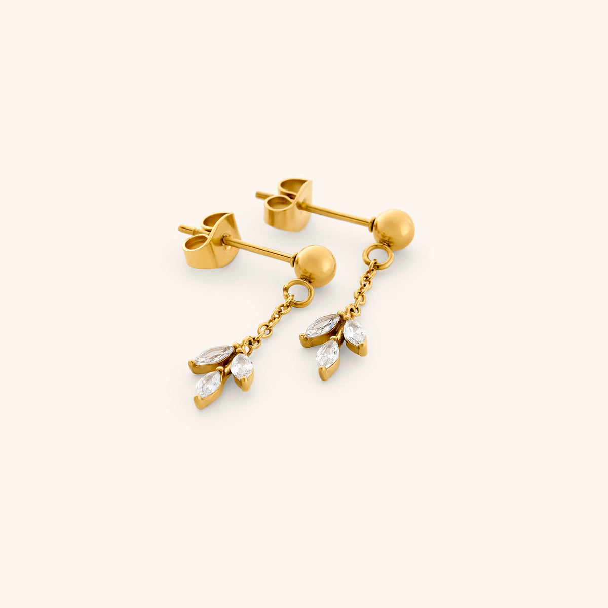 The Pavé Raining Olive Branch Drop Earrings by Nominal, featuring polished 18k gold-plated ball studs suspending delicate chains with sparkling pavé crystal leaf clusters, displayed on an off-white background.