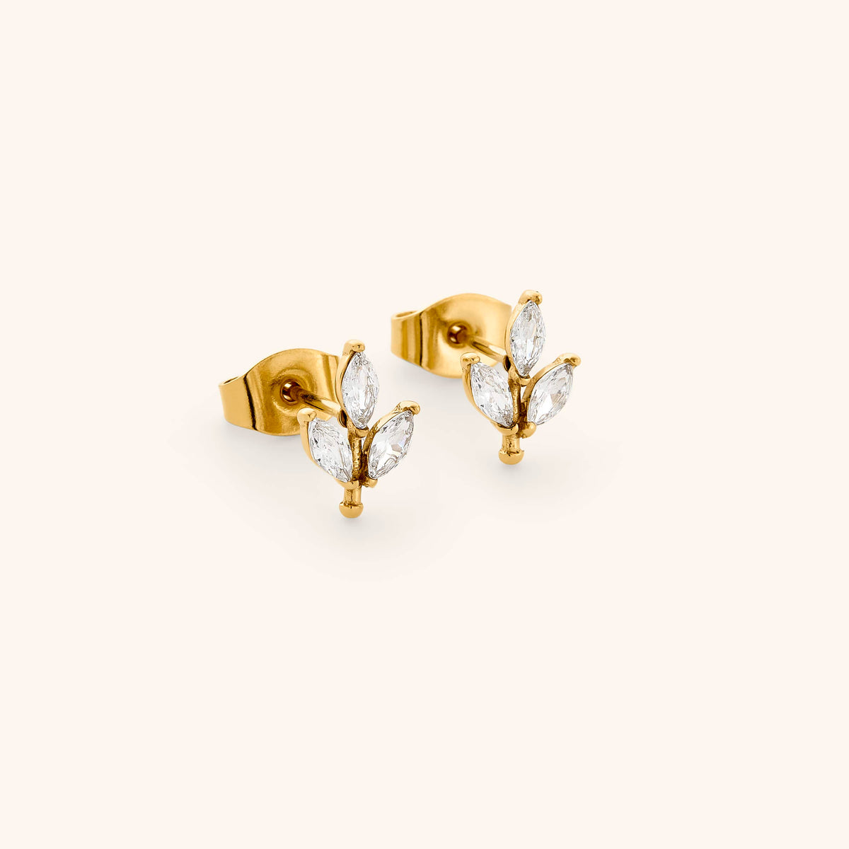 The Pavé Olive Branch Studs by Nominal, featuring sparkling marquise crystal olive leaves set in 18k gold plating on post-back stud earrings, displayed on an off-white background.
