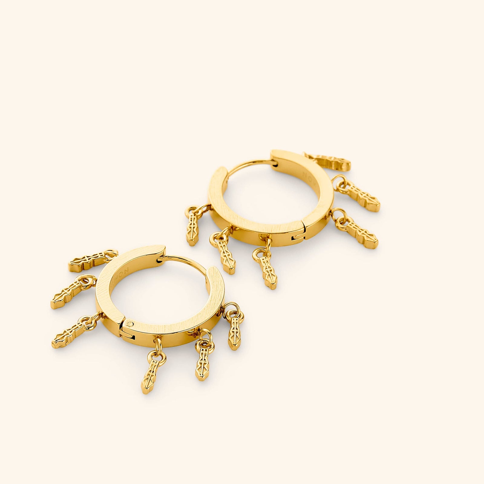 A pair of 18k gold plated chunky hoop earrings with tatreez patterns hanging beneath, each one carved with the traditional Palestinian embroidery