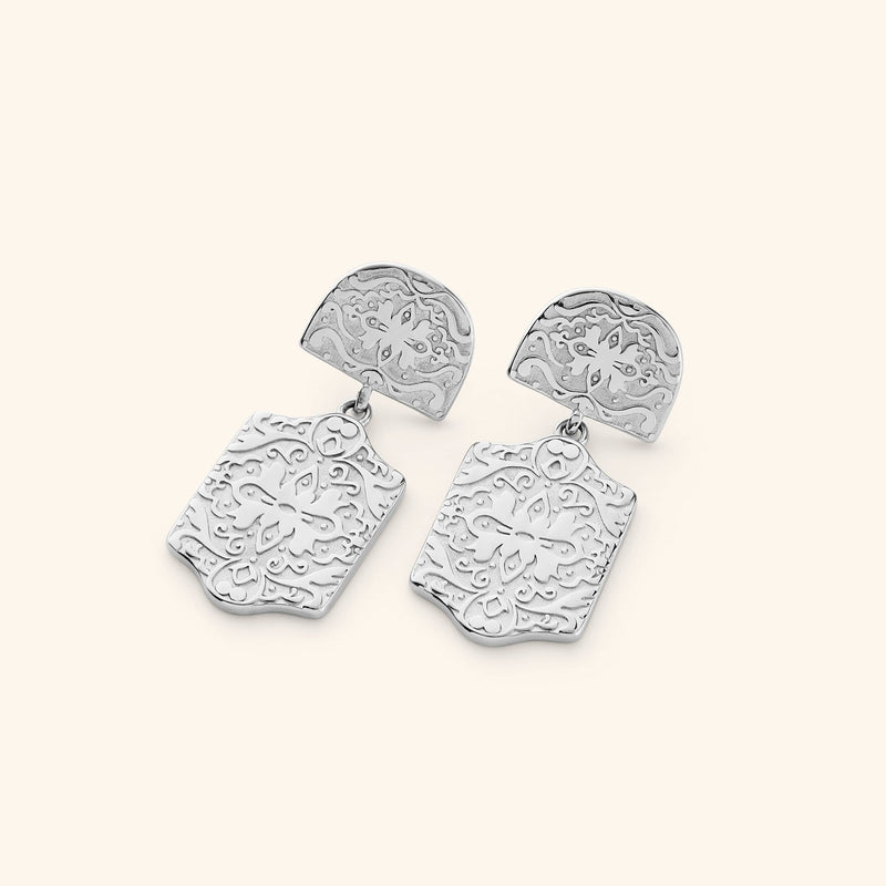 Pair of silver Roaming Earrings featuring engraved floral and vine motifs on both the rounded top and dangling rectangular plates pimage_ displayed against a light background.
