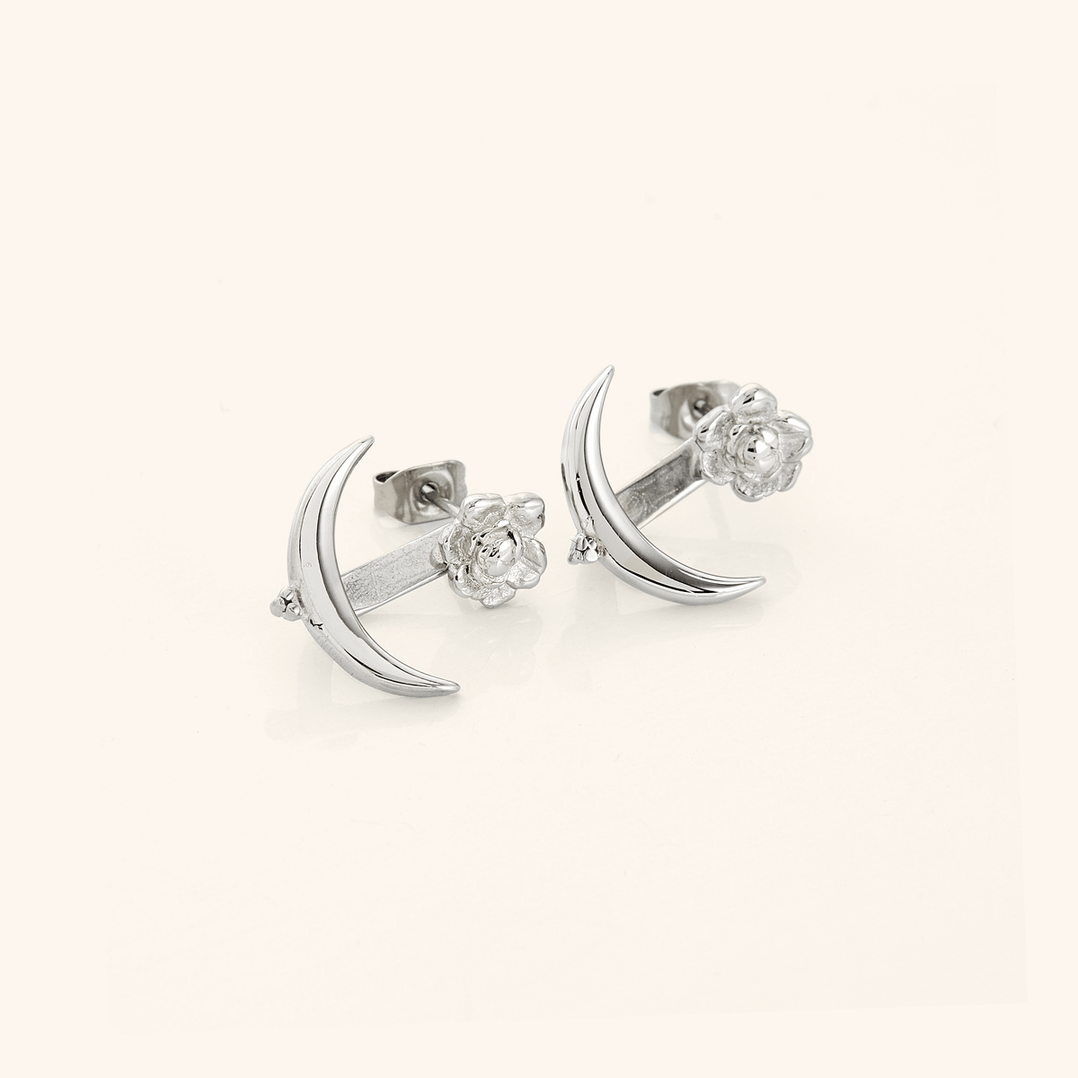 A pair of silver earrings that feature a damask rose and crescent shape design.