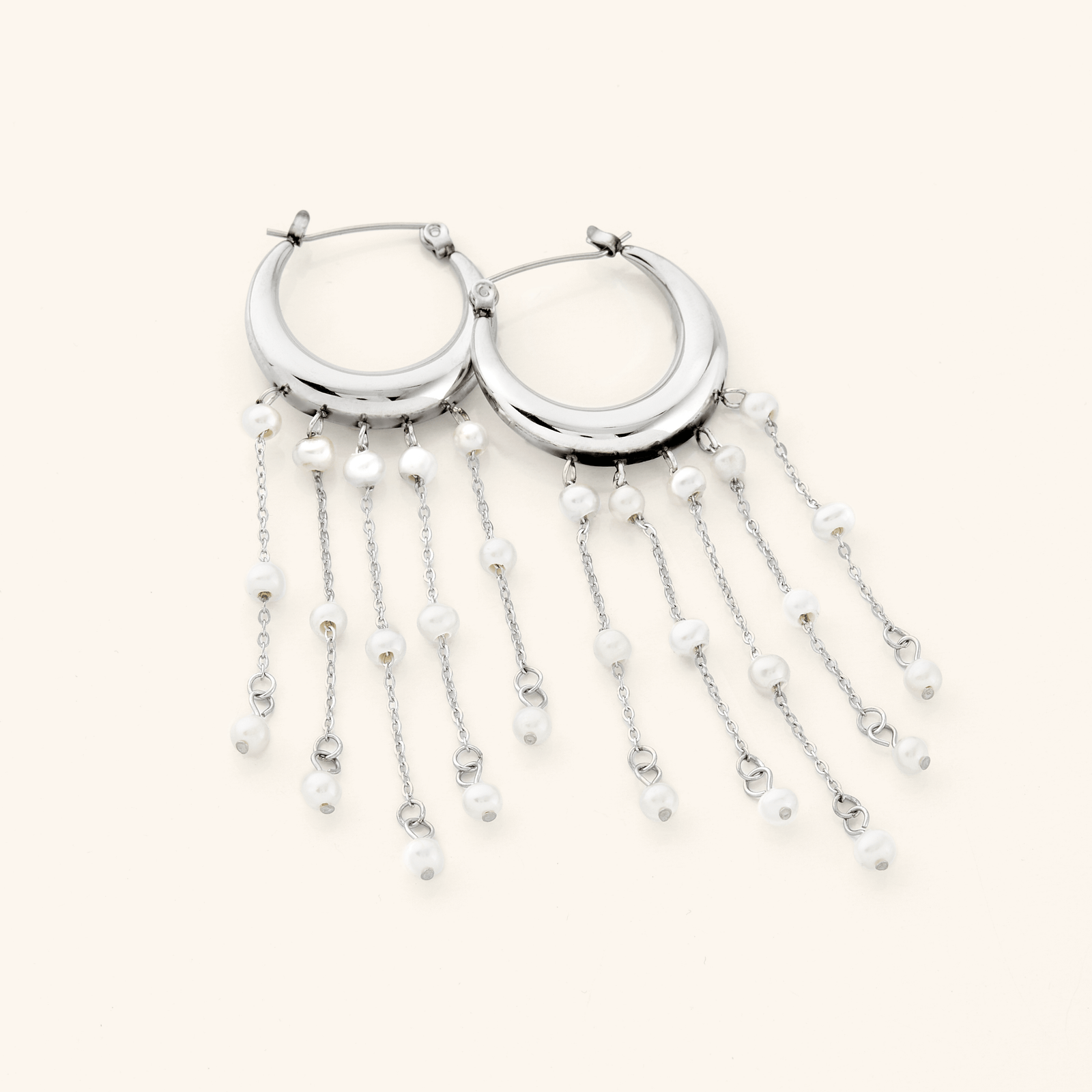A pair of silver earrings crafted in the shape of a delicate crescent, this hoop gracefully extends to embrace a cascade of raining pearls at its bottom.