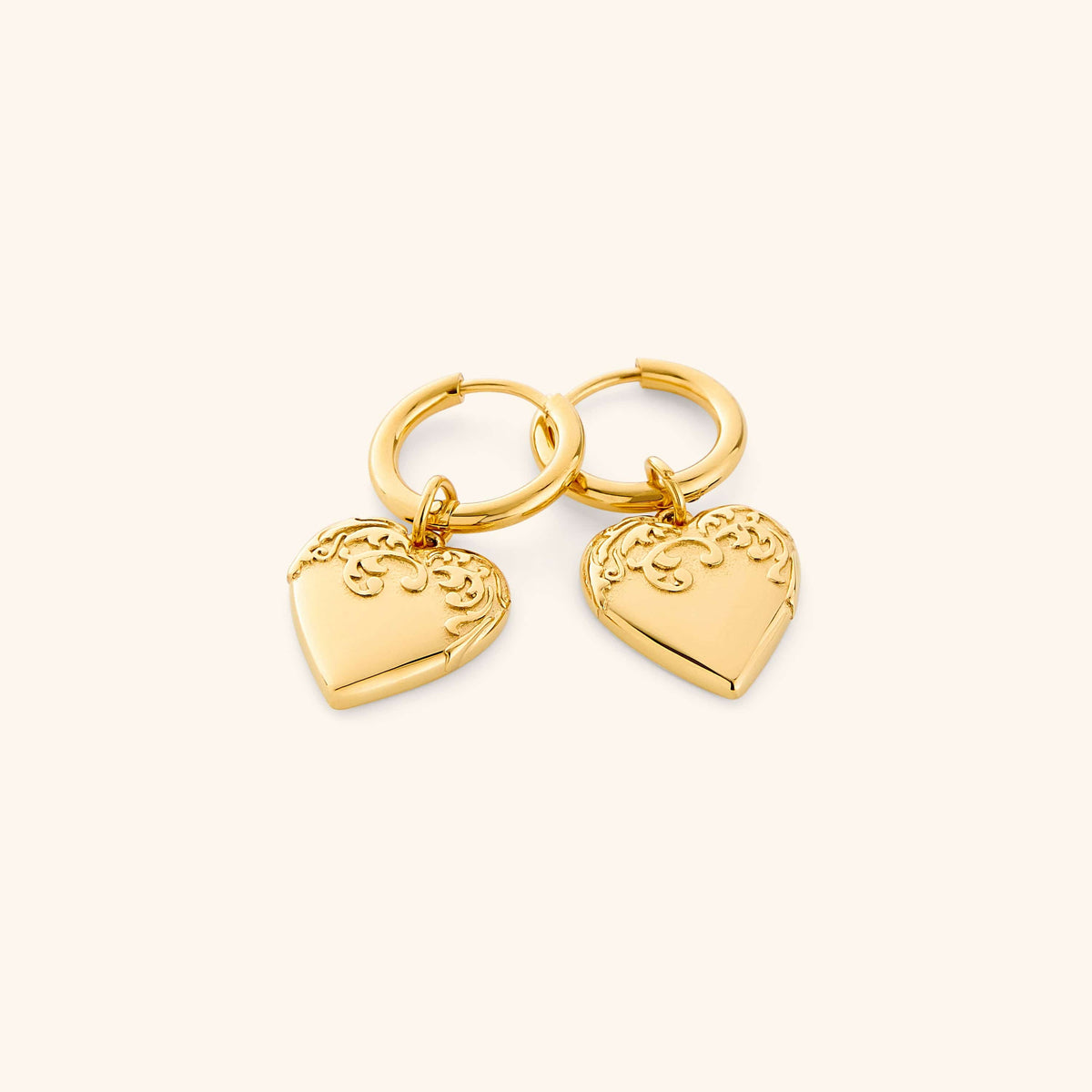 Gold hoop earrings with heart-shaped charm on a white background