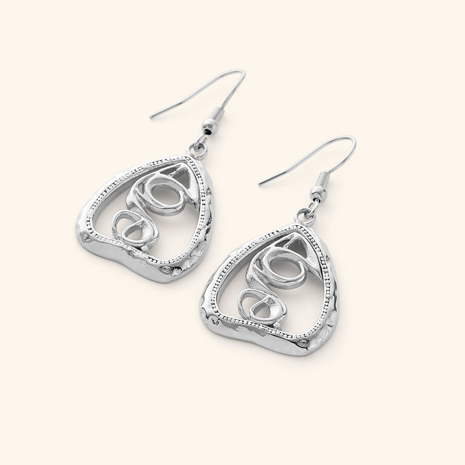 A pair of silver "Hub (Love)" earrings. The earrings feature a unique, abstract design with swirling lines enclosed within a roughly triangular frame. The metal is a warm gold color, and the background is a soft, light beige. The image is a product shot, likely showcasing the design and craftsmanship of the earrings. The text "This image might show: Hub (Love) Earrings" confirms the product name.