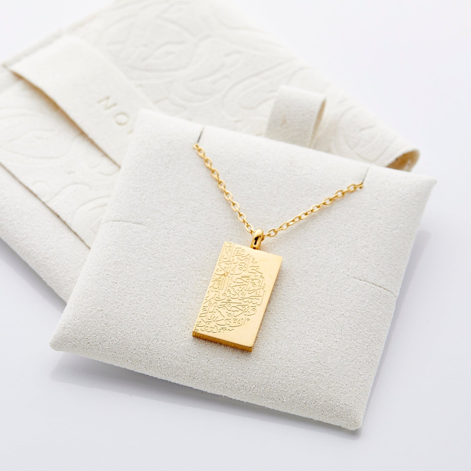 The gold "Tranquility in Them" Necklace | His & Hers displayed on the soft, light colored jewelry cushion.