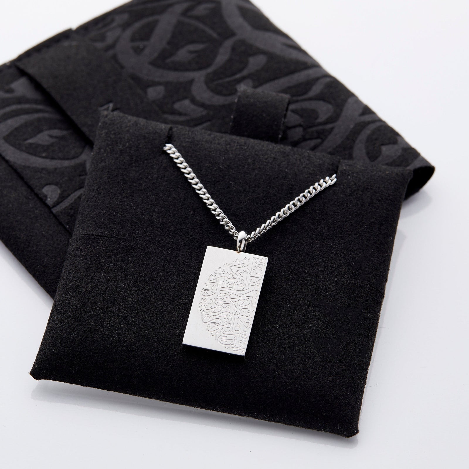 The silver "Tranquility in Them" Necklace | His & Hers displayed on the soft, dark colored jewelry cushion.