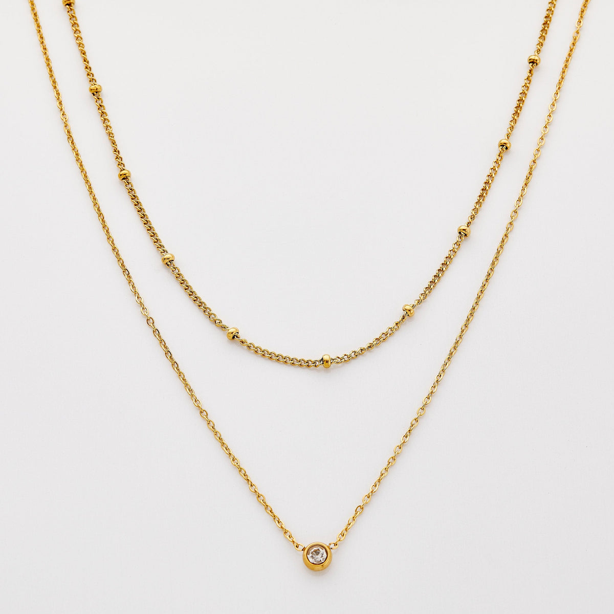 Gold necklace set featuring a bead-accented chain layered with a solitaire bezel-set pendant necklace.