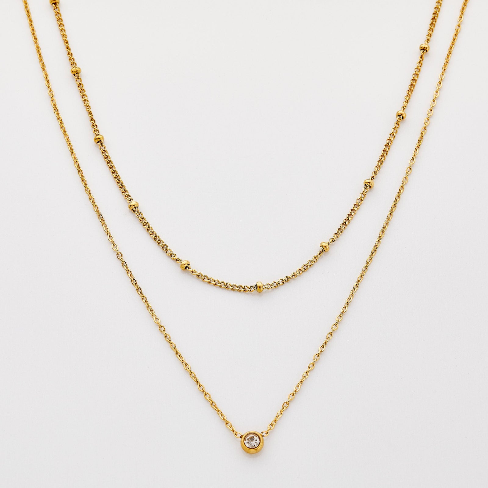 Gold necklace set featuring a bead-accented chain layered with a solitaire bezel-set pendant necklace.