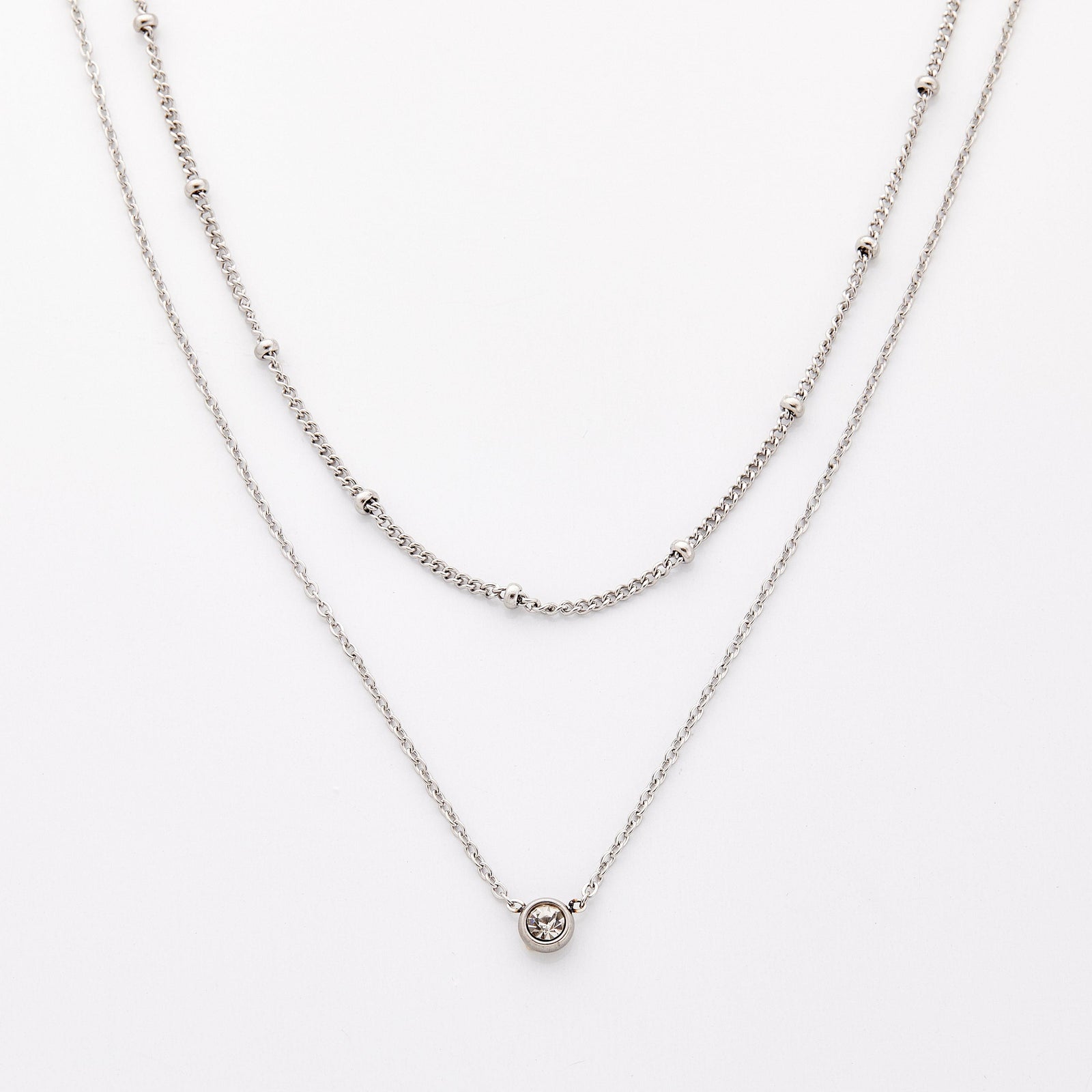 Silver necklace set featuring a bead-accented chain layered with a solitaire bezel-set pendant necklace.