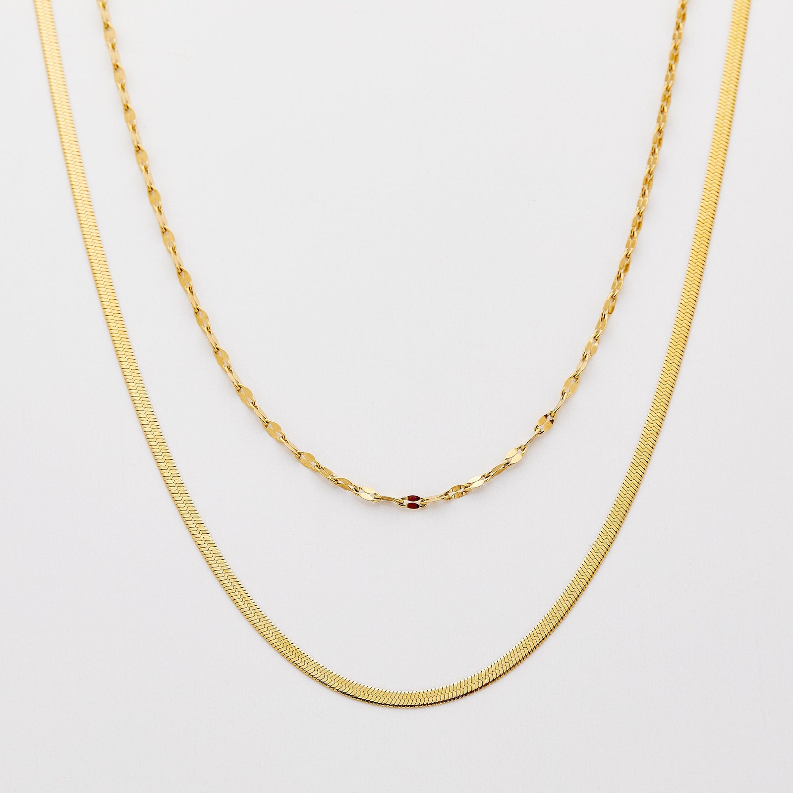 Photo of two 18k gold plated necklaces. This set features two elegant chains, the slant-pattern Herringbone Chain, and the dainty flake-like Flutter Chain.