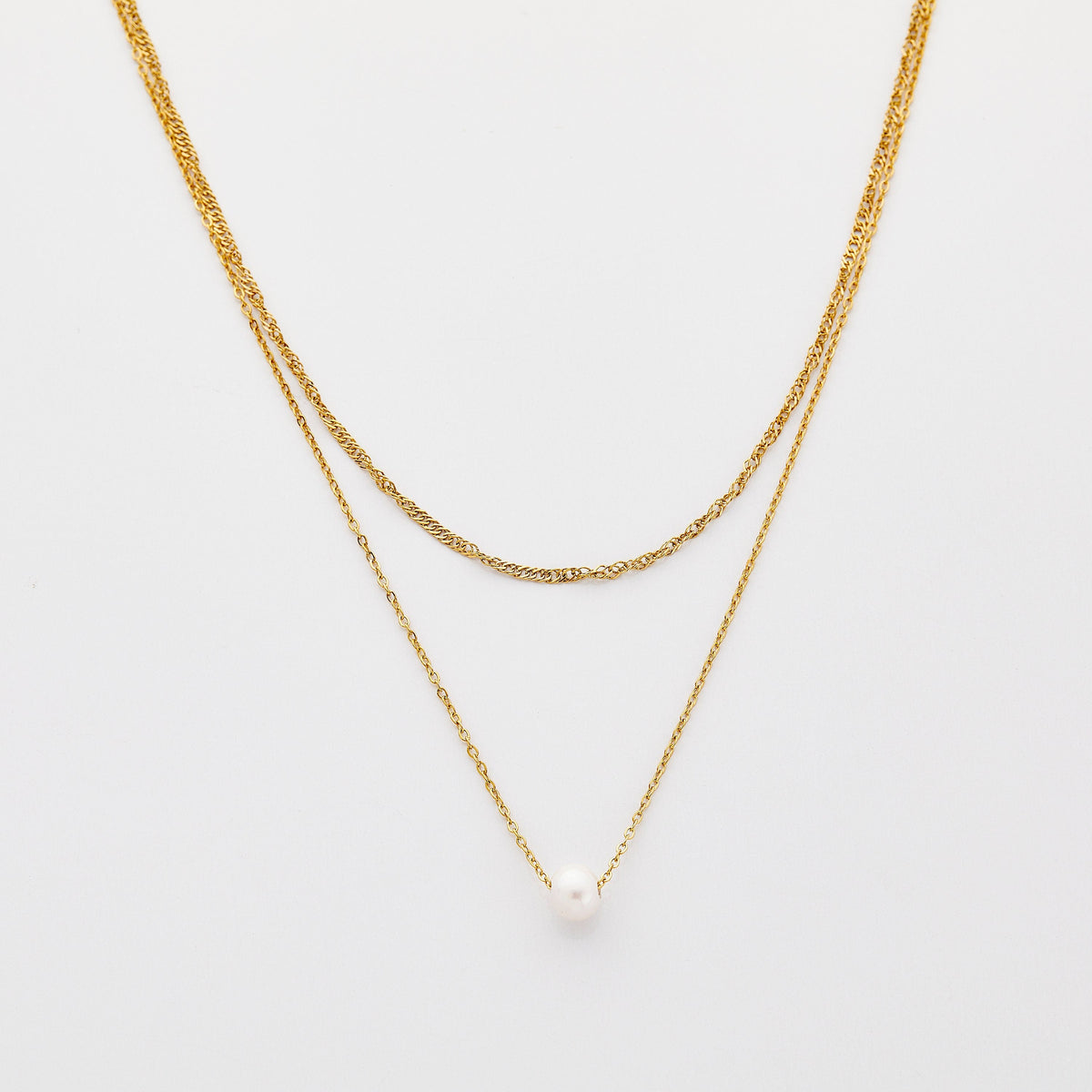 Layered gold necklaces featuring a twisted chain and a delicate chain with a single white pearl pendant, displayed on a neutral beige background.