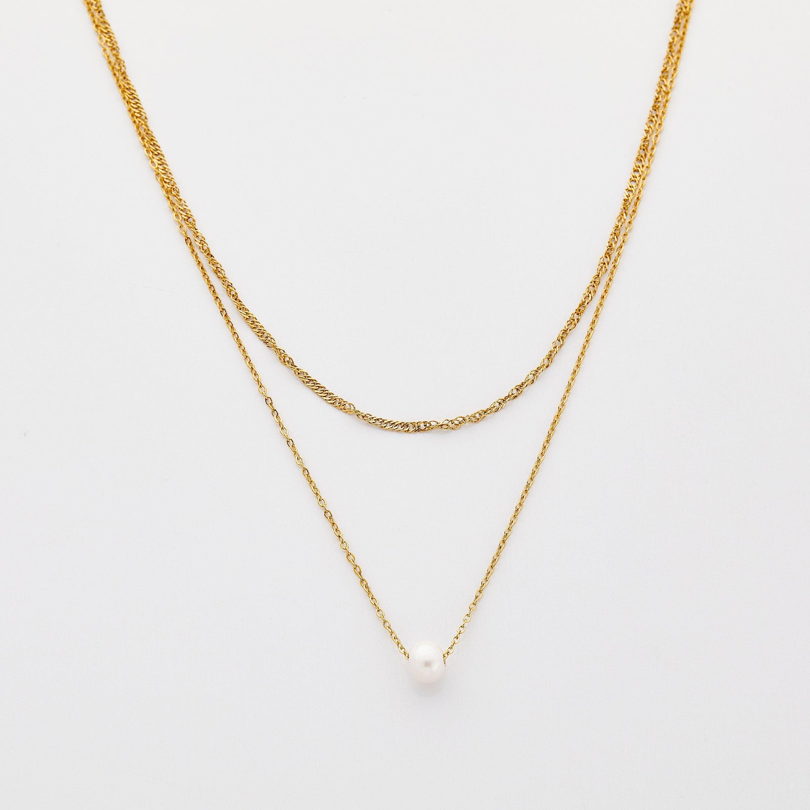 Layered gold necklaces featuring a twisted chain and a delicate chain with a single white pearl pendant, displayed on a neutral beige background.