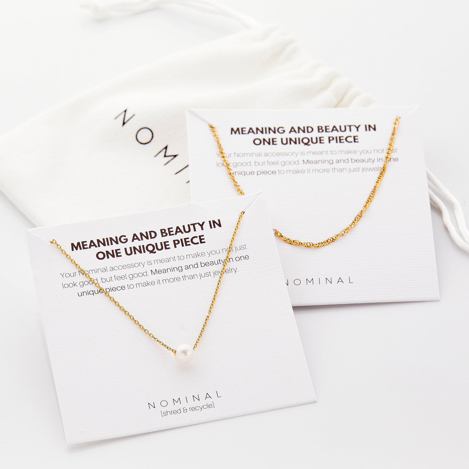 Gold rope chain necklace and pearl pendant necklace displayed on branded Nominal cards reading 'Meaning and beauty in one unique piece,' with a white Nominal pouch in the background.