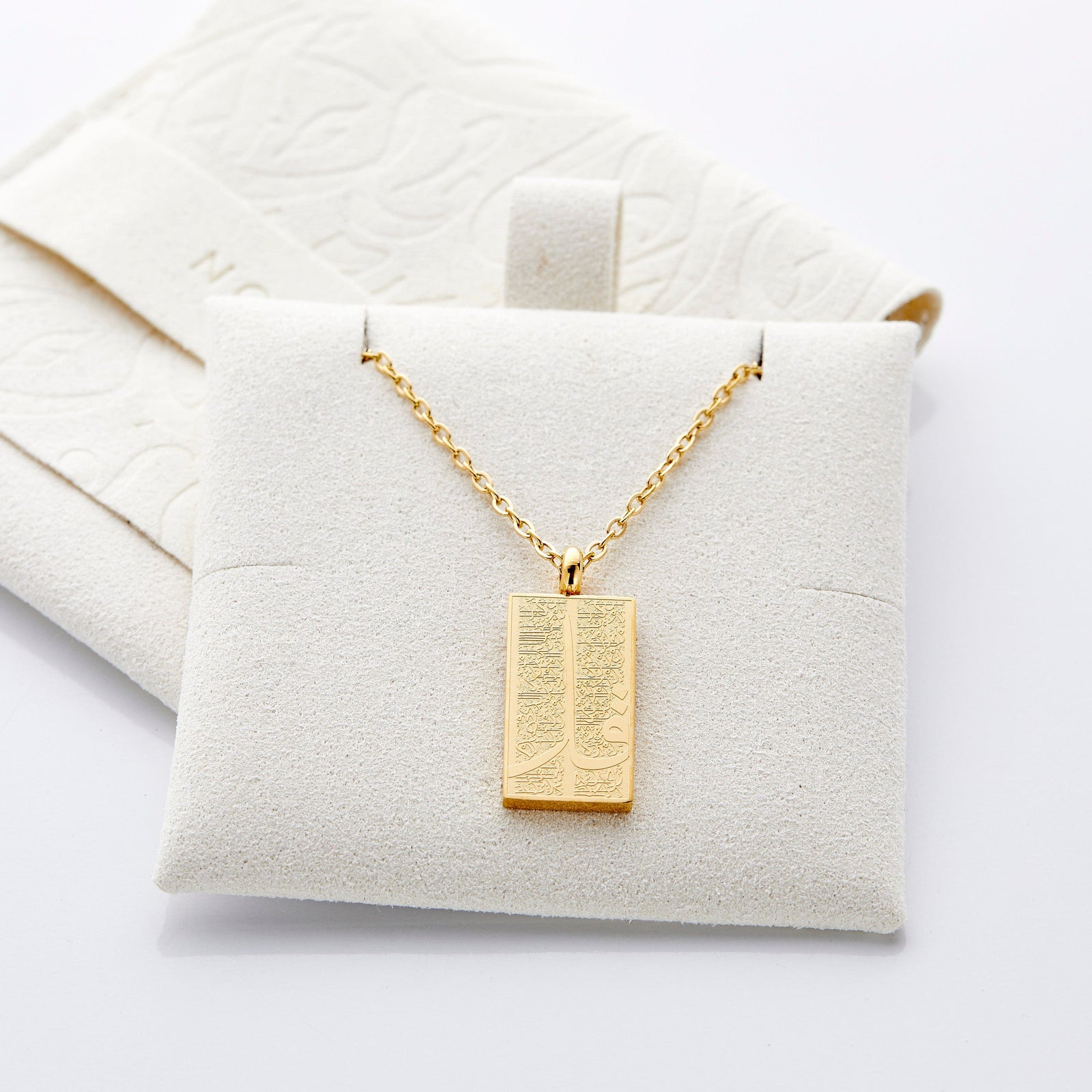 The gold '4 Qul' Tag Necklace | Women displayed on a soft, light colored jewelry cushion.