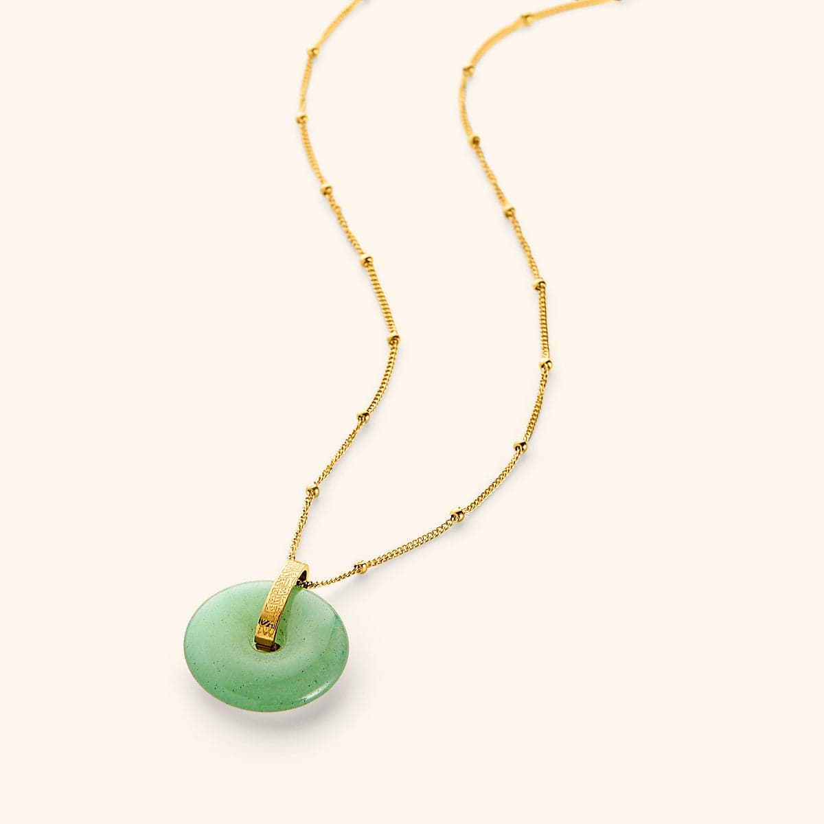 A round green aventurine stone pendant on a gold beaded chain, with engraved Arabic calligraphy on the gold bail.