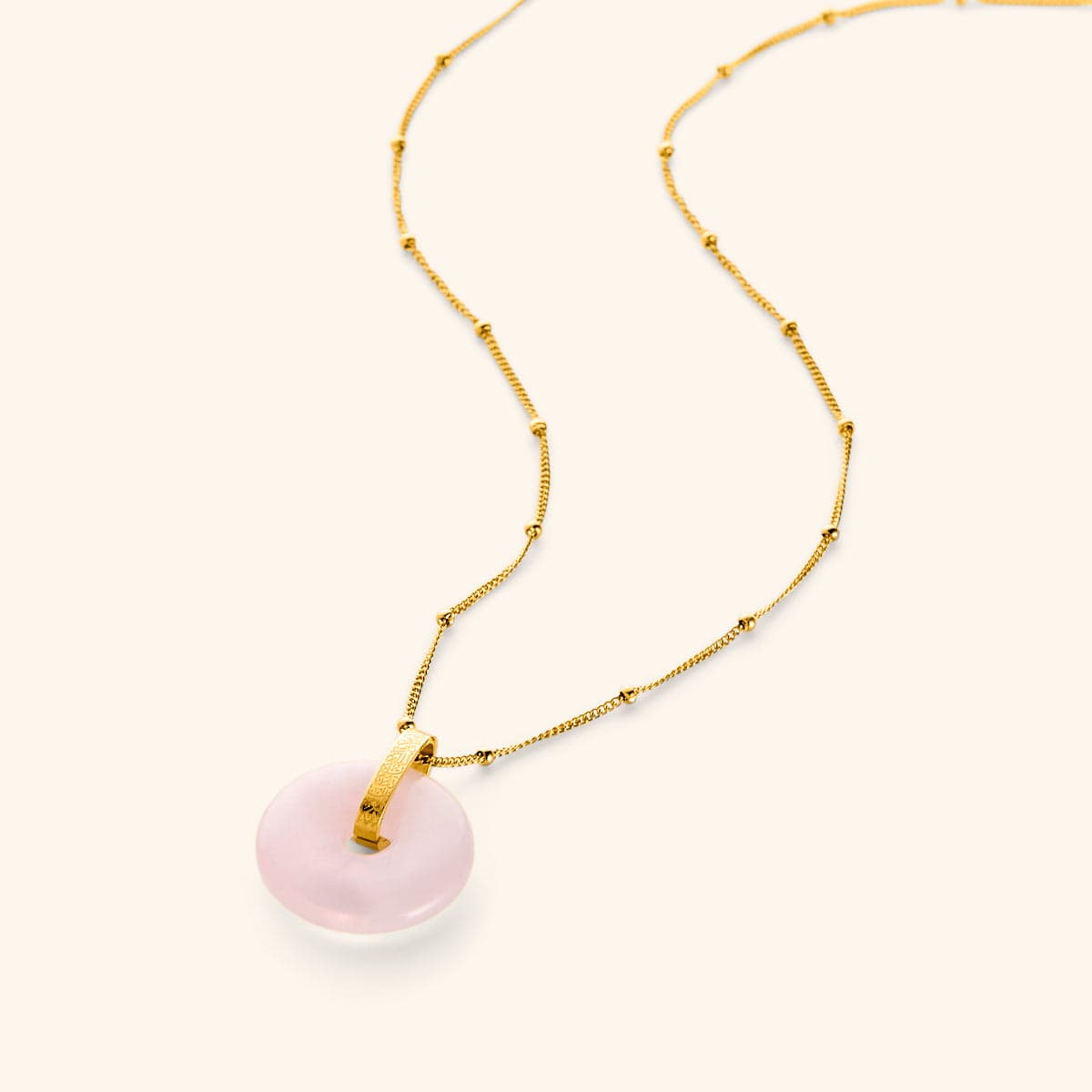 A round rose quartz stone pendant on a gold beaded chain, with Arabic calligraphy engraved on the gold bail.