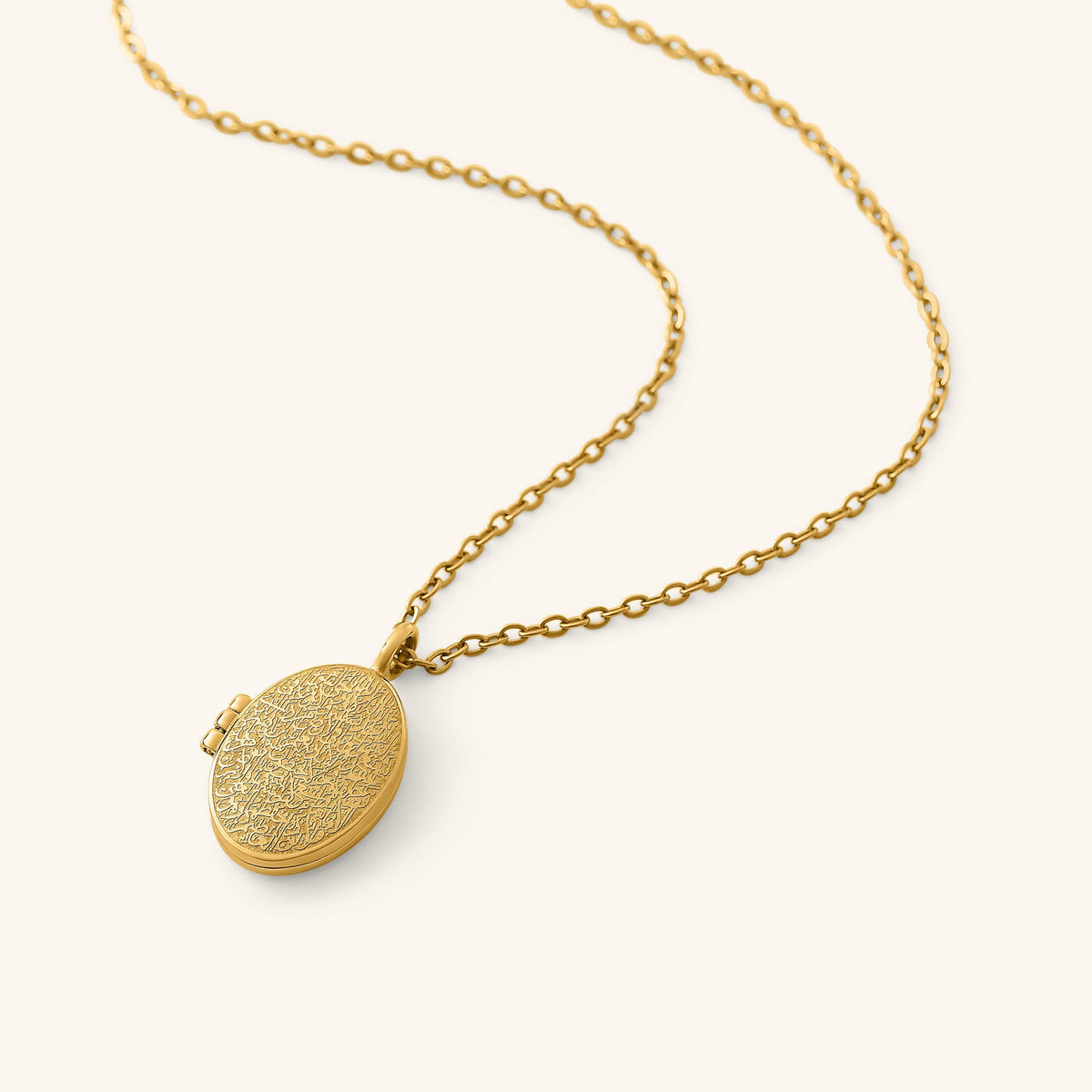 Gold oval locket engraved with detailed Ayatul Kursi calligraphy on the front, hanging from a gold chain on a neutral background.
