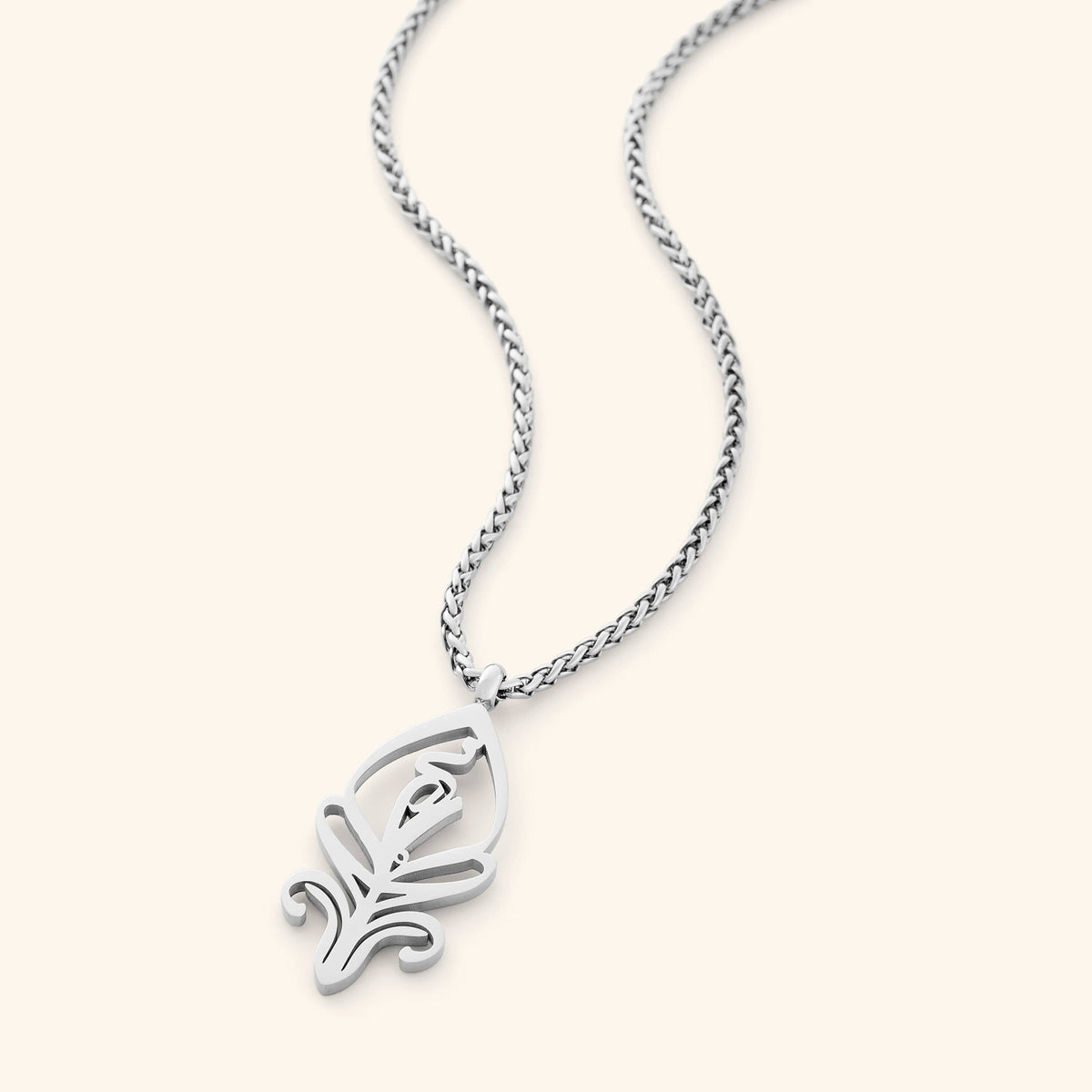 A delicate silver-plated chain necklace featuring a stylized, oval pendant with intricate cut-out details. The necklace is displayed against a light beige background.
