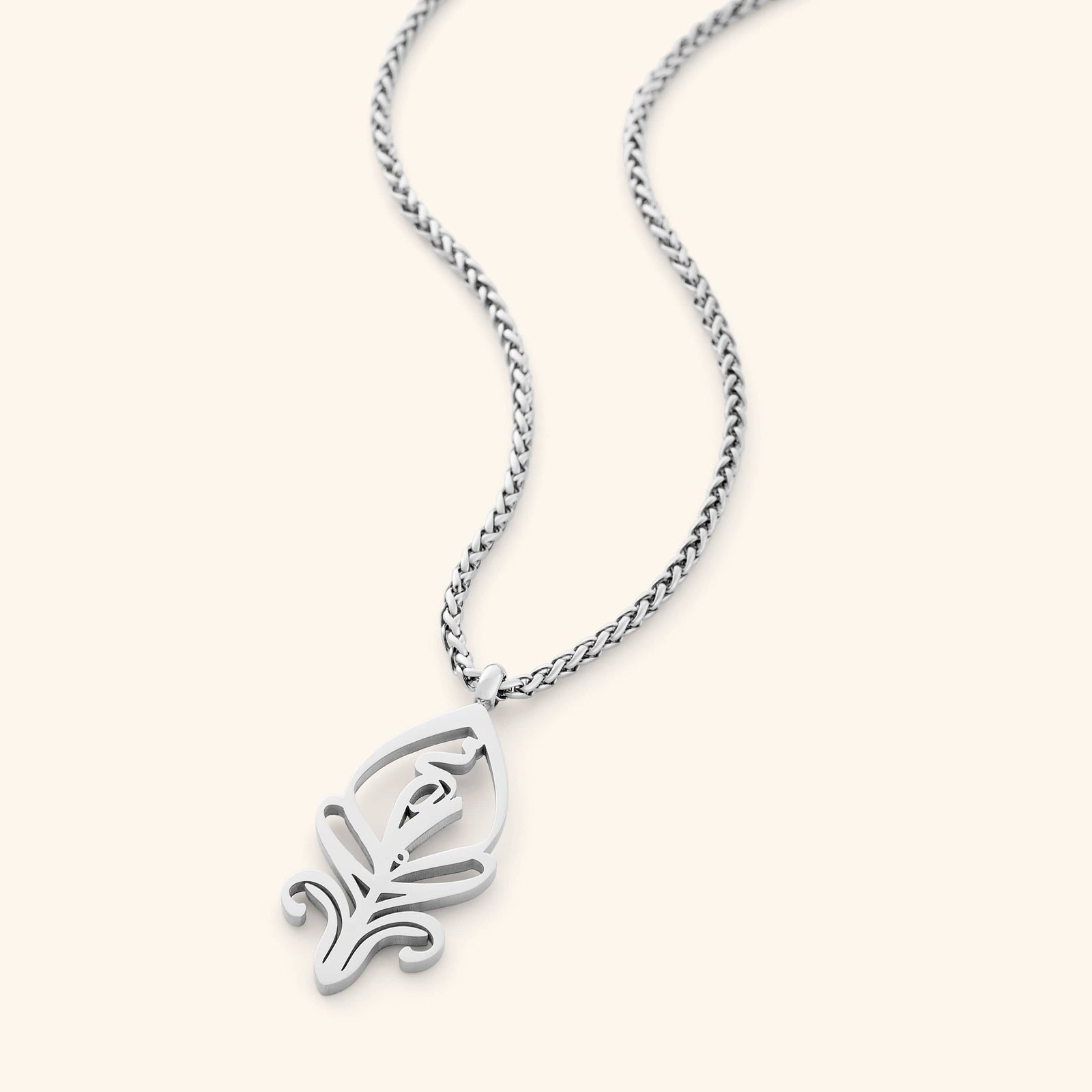 A delicate silver-plated chain necklace featuring a stylized, oval pendant with intricate cut-out details. The necklace is displayed against a light beige background.