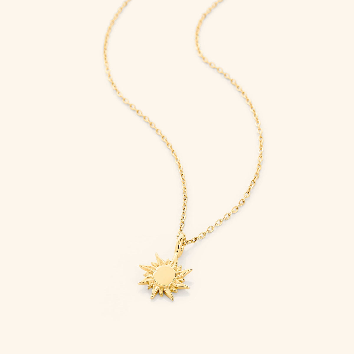 Flat lay of an 18k gold plated necklace with a sun-shaped pendant.