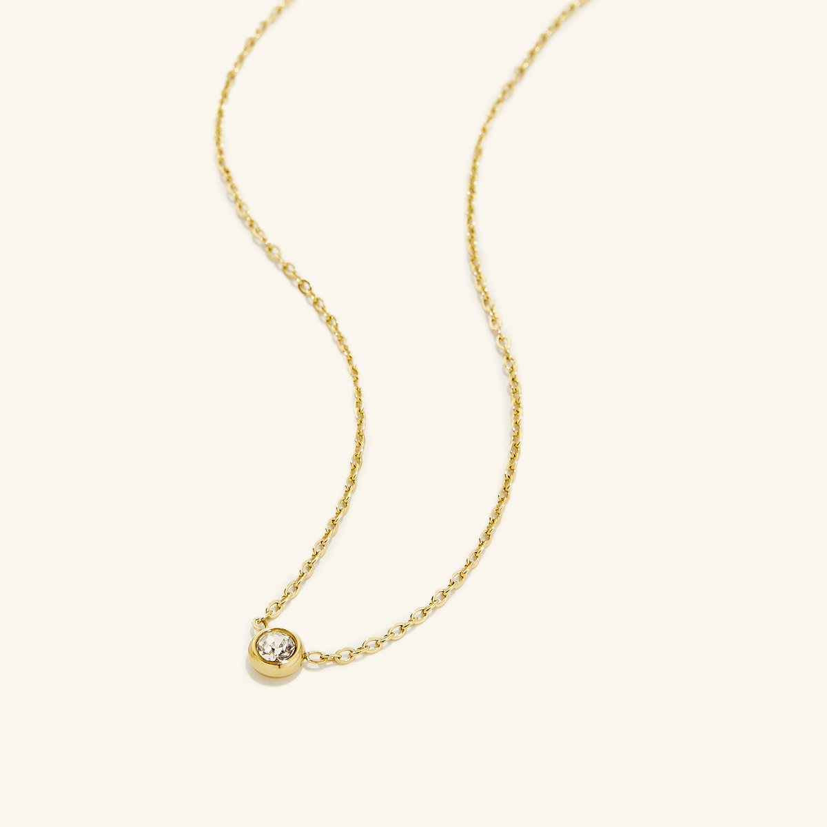 Photo of an 18k gold plated necklace that is laid flat on a light background. The Bezel Necklace carries a singular radiating gem.