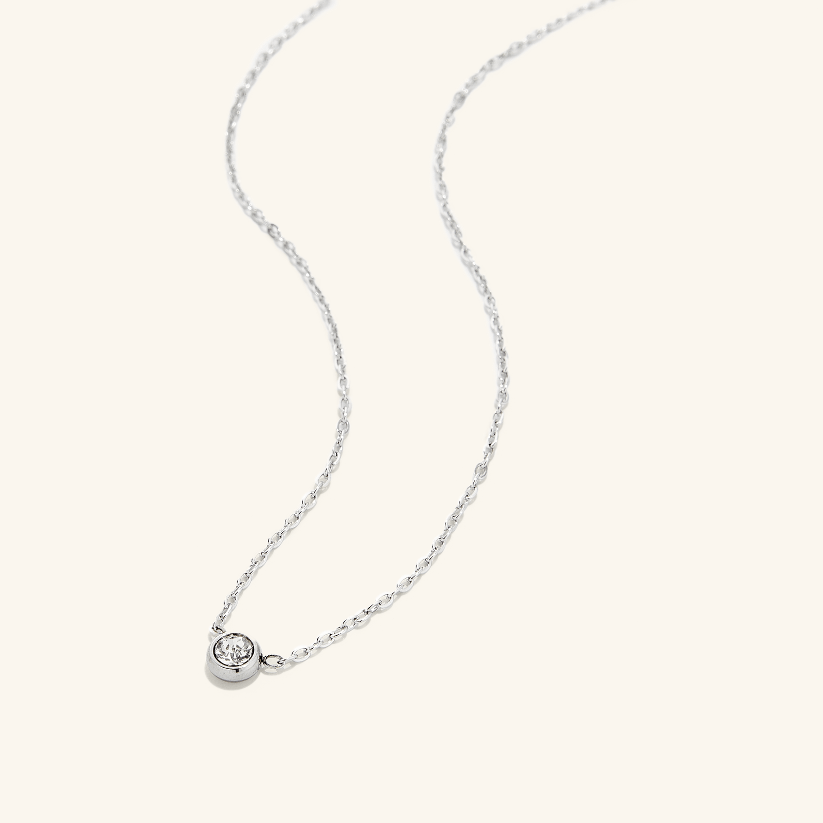 Photo of a silver necklace that is laid flat on a light background. The Bezel Necklace carries a singular radiating gem.