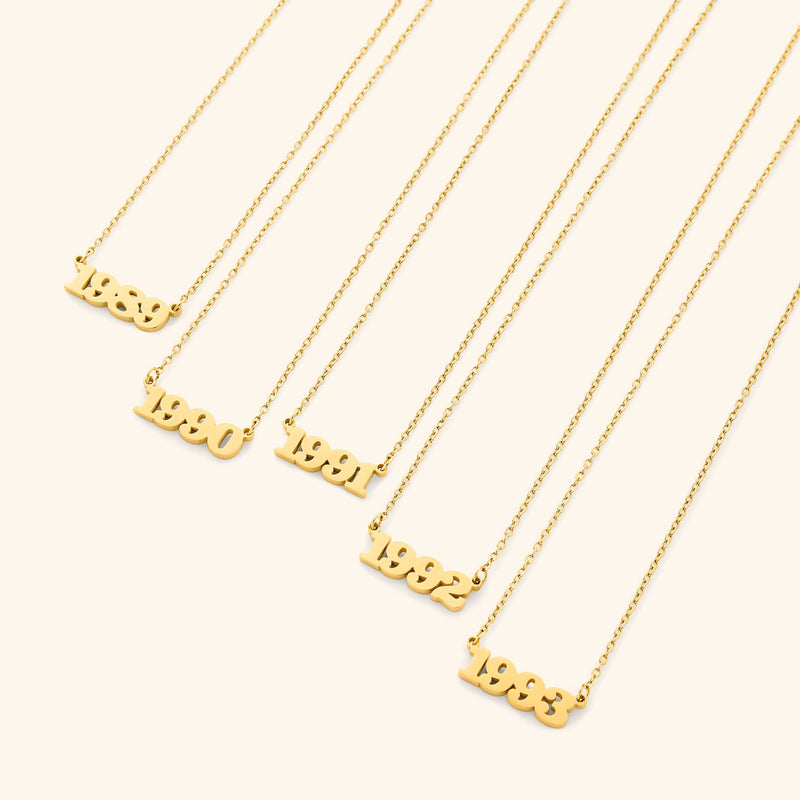 Gold necklace with english number pendants representing birth years on a light background