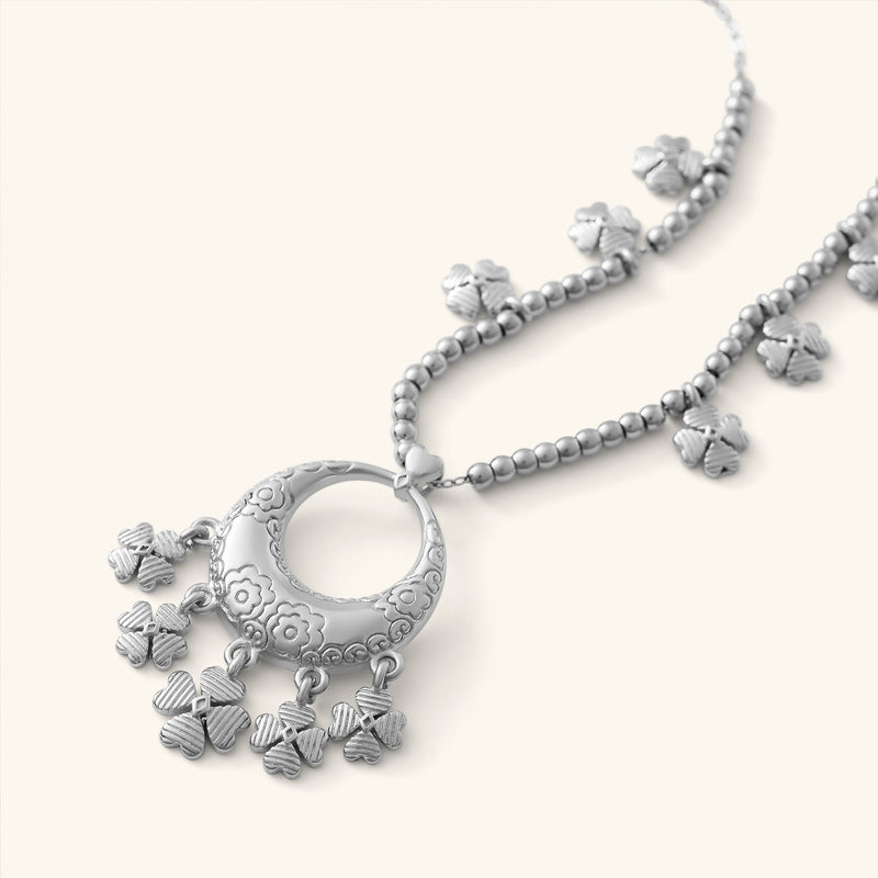 Close-up of the Levantine Garden Necklace pimage_ featuring a silver pendant engraved with floral Levantine patterns and adorned with multiple dangling clover-shaped charms. The pendant hangs from a beaded gold chain with additional clover charms spaced along it.
