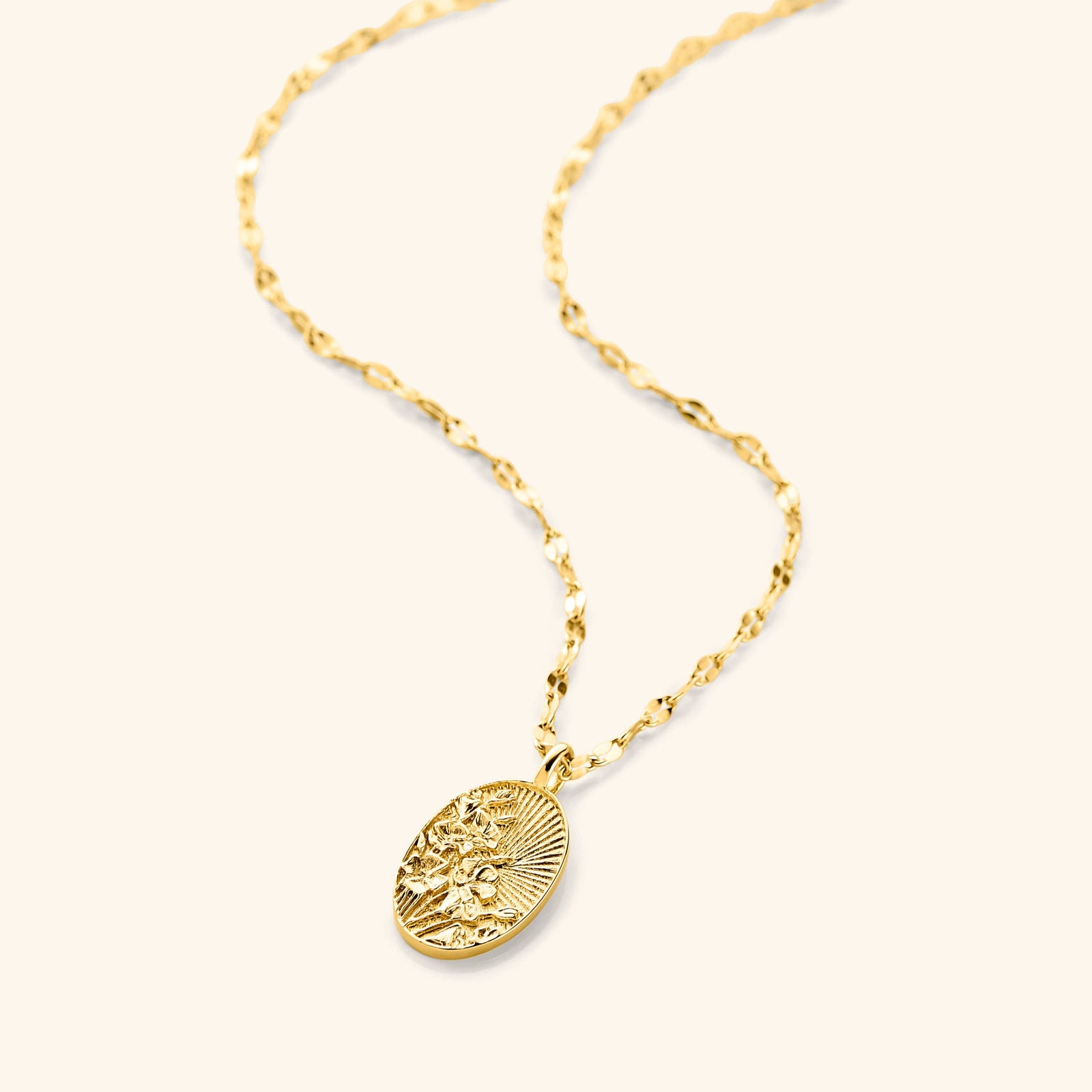 An 18k gold plated necklace that  features a molded bouquet of poppies, the national flower of Palestine, on a disc that features sun rays with a vintage finish pendant hanging on a gold plated flutter chain.